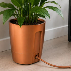 Copper-colored planter with a lush green houseplant indoors; a power cord extends from the base on the floor.